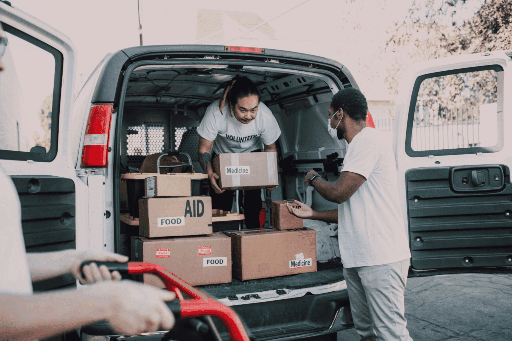 Volunteers unloading a van filled with boxes labeled food, aid, and medicine to support community relief efforts.
