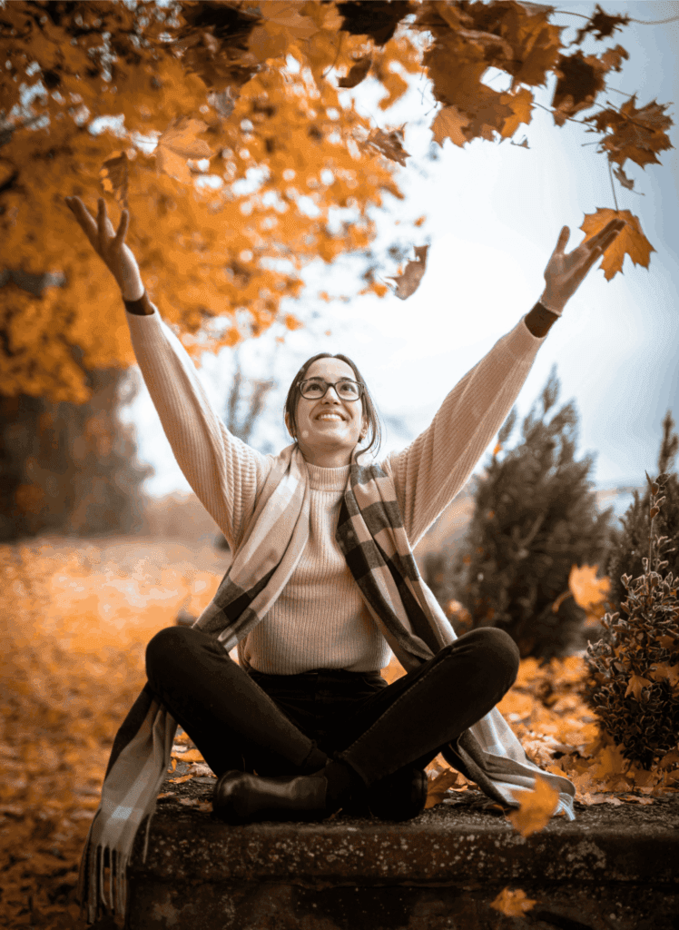 Happy women sitting amongst orange autumn leaves smiling into the sky 