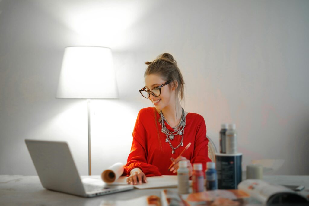 Smiling woman in red shirt working on a laptop at a desk