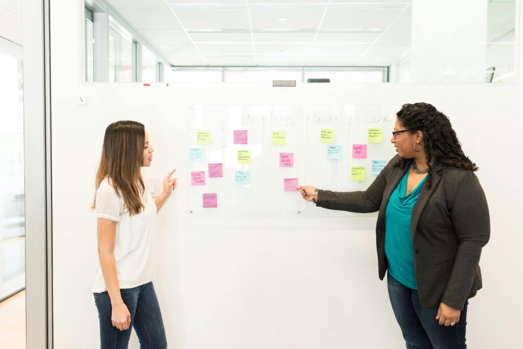 Coworkers collaborating on project planning with sticky notes on a whiteboard for task management and workflow strategy.
