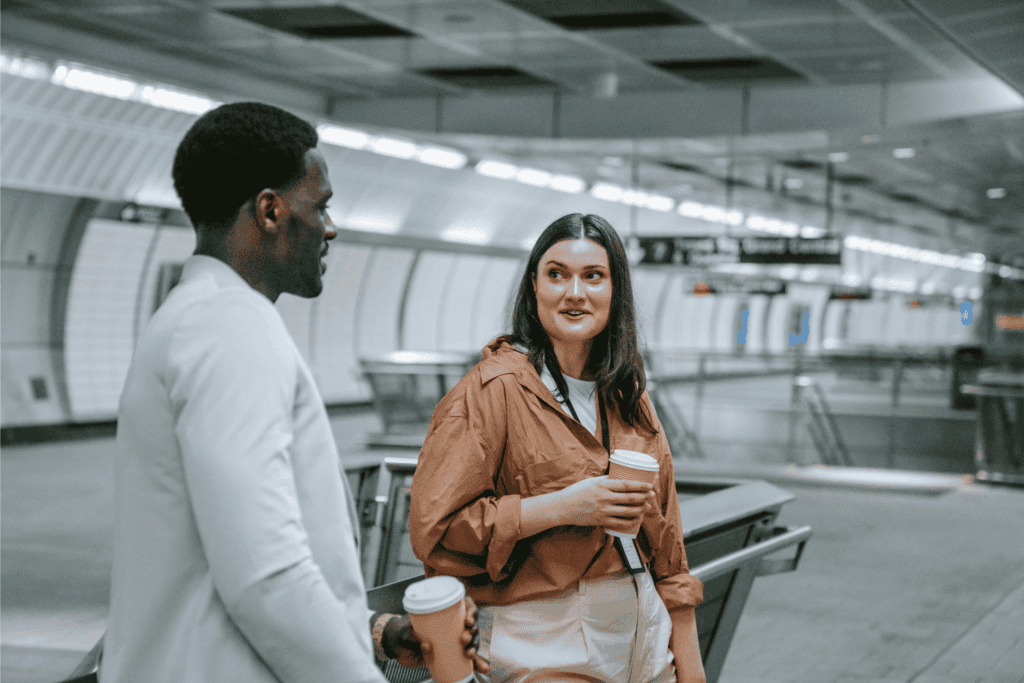 Coworkers having a casual conversation with coffee cups while waiting in a modern subway station.