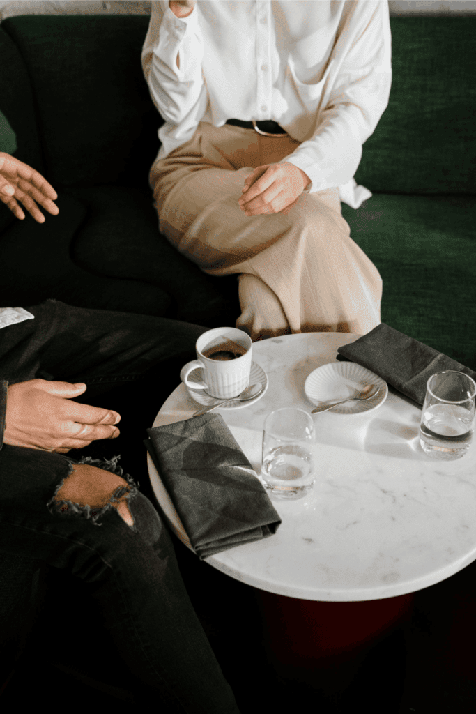 Two people sitting at a café table with coffee and water, having a conversation.