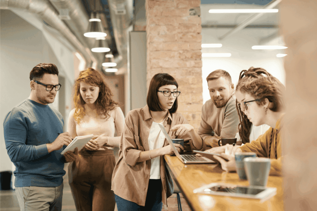 Team of coworkers gathered around a laptop in a modern office, collaborating on a project. 