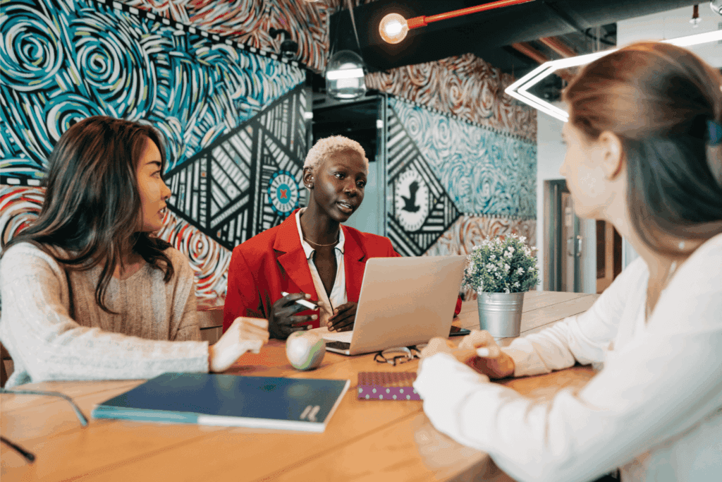 Three coworkers having a meeting in a modern office with colorful mural walls and a laptop on the table.