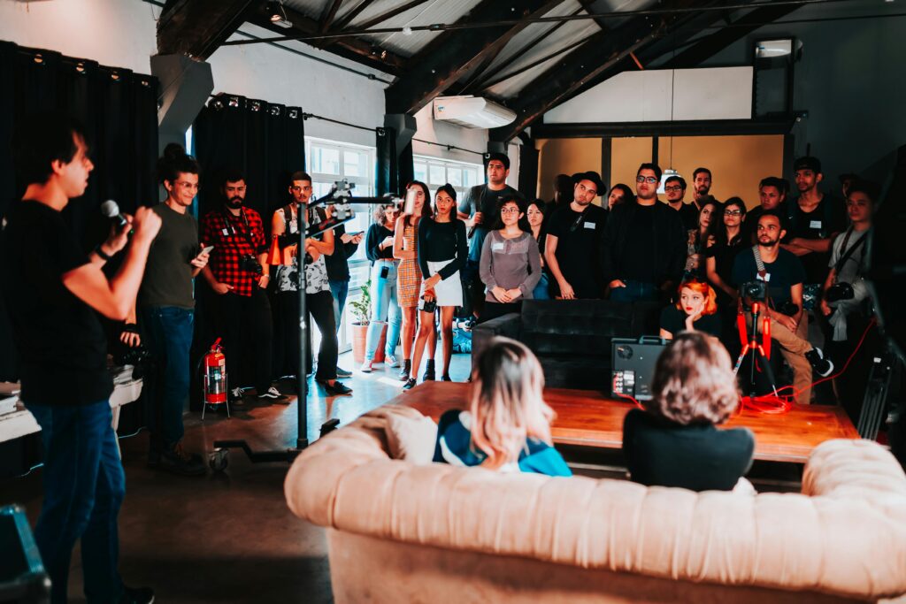 A man speaks into a microphone while a diverse group of people attentively listen in a casual indoor event space.