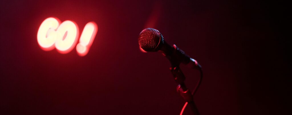 Microphone on stage under red lighting with glowing "Go!" sign in the background.