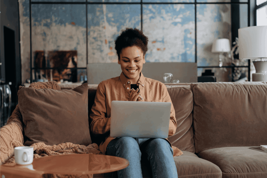 Smiling woman sitting on a couch working on a laptop in a cozy modern living room