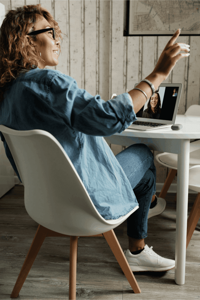 Smiling woman in casual denim having a video call on her laptop at home office desk