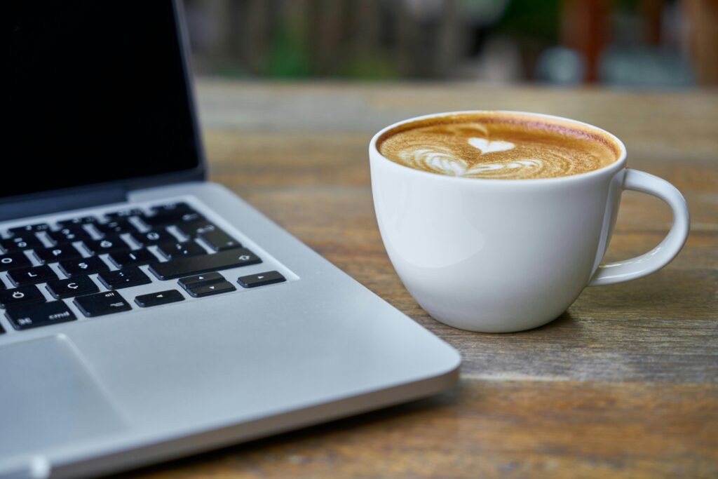 Laptop and latte art coffee cup on a rustic wooden desk, perfect for remote work and productivity