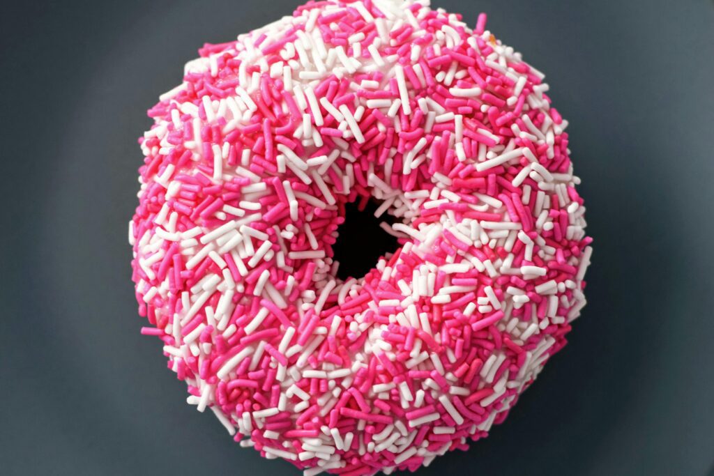 Pink frosted donut covered in white and pink sprinkles on a dark background