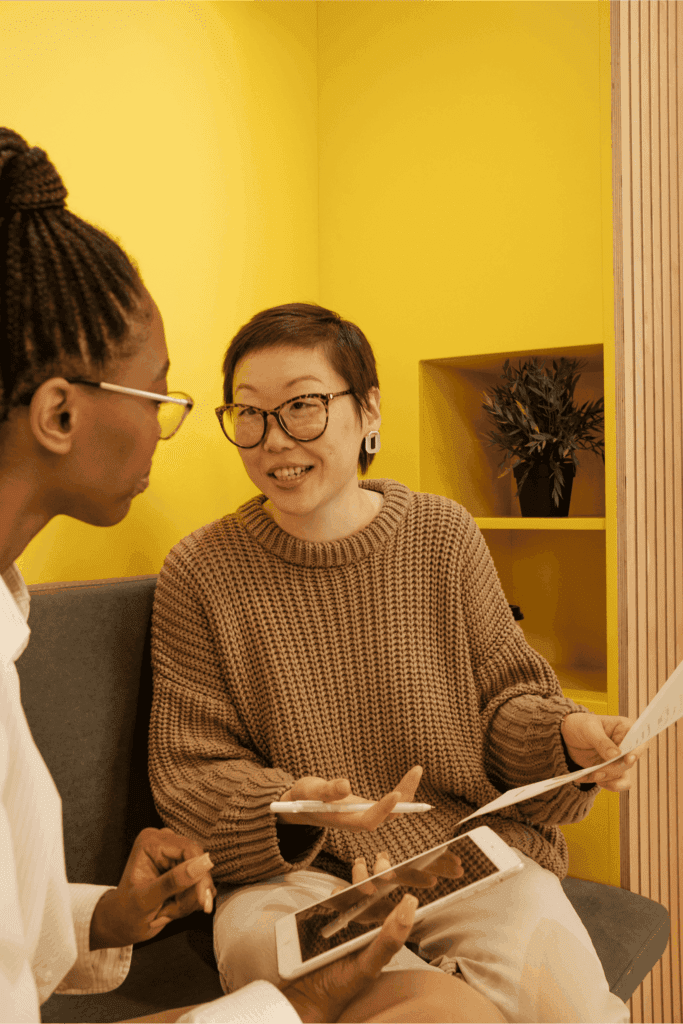 Two colleagues having a discussion with documents and a tablet in a modern office with bright yellow wall