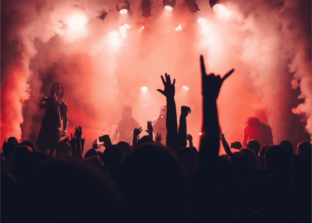 Energetic rock concert with a crowd raising hands in front of a smoke-filled stage with red lighting