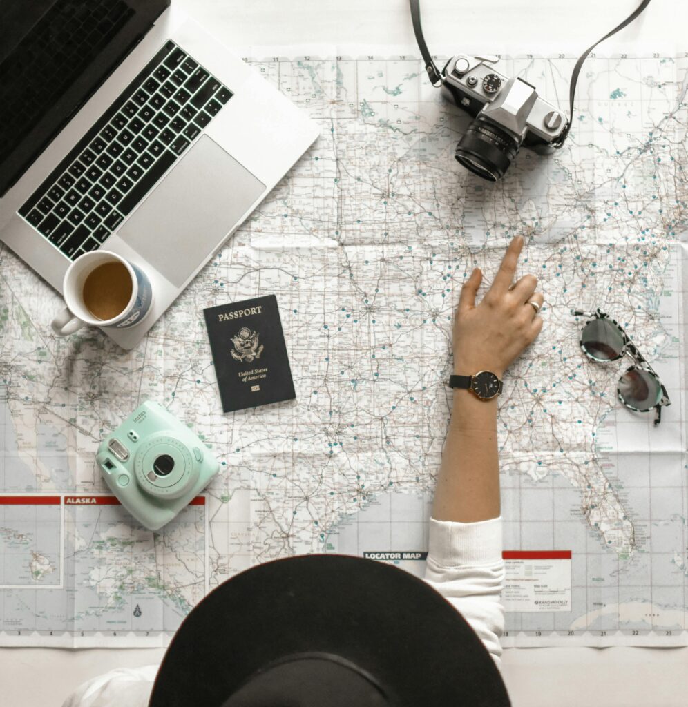 Traveler planning a trip with a map, passport, camera, laptop, coffee, and instant camera on the table