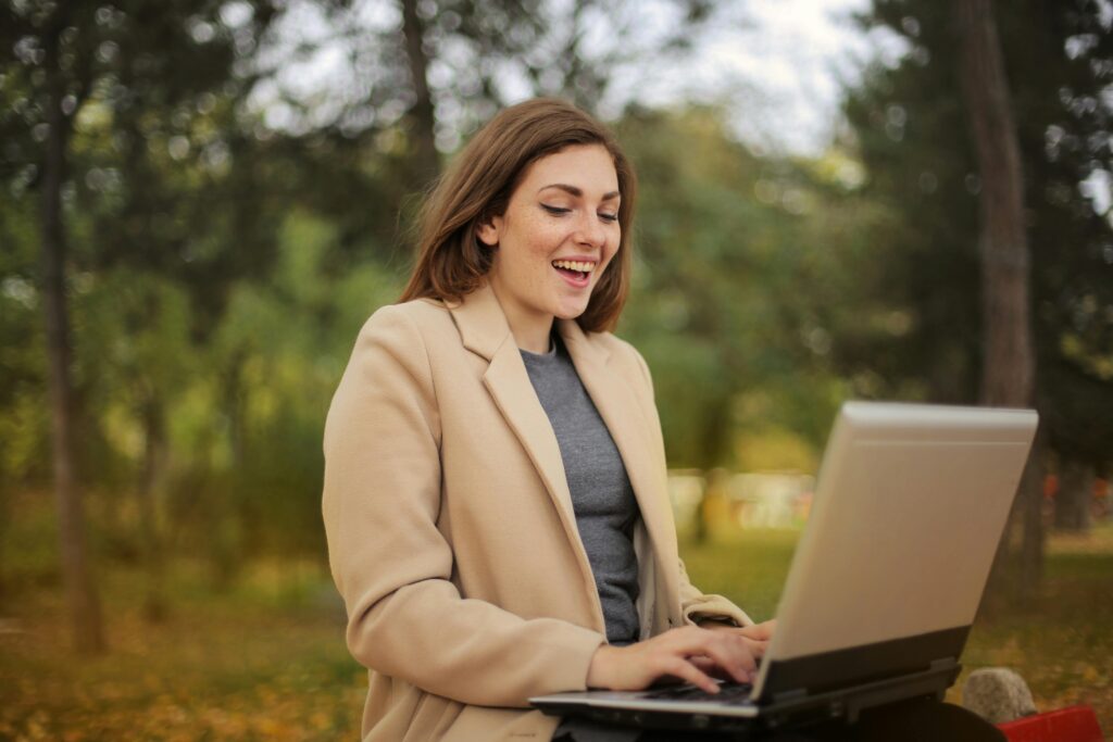Smiling woman working on a laptop outdoors in a park setting