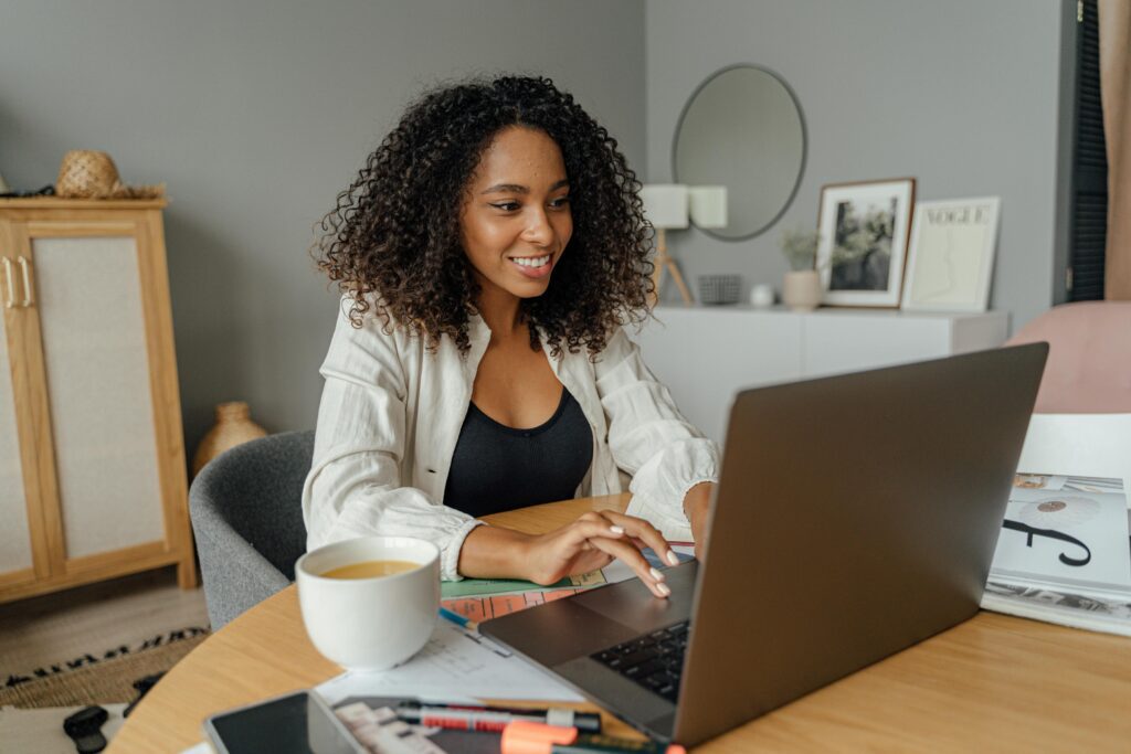 Smiling woman working on a laptop from her home office with coffee and notes on the desk