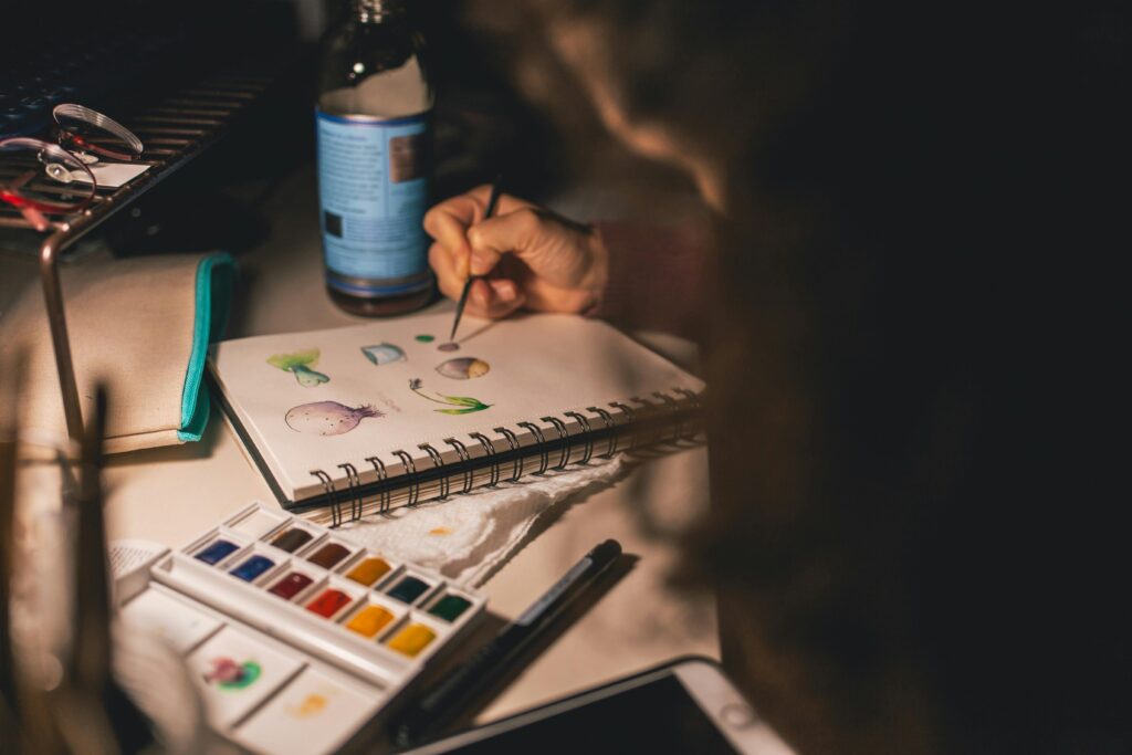 Artist painting colorful watercolor illustrations in a sketchbook at a creative workspace
