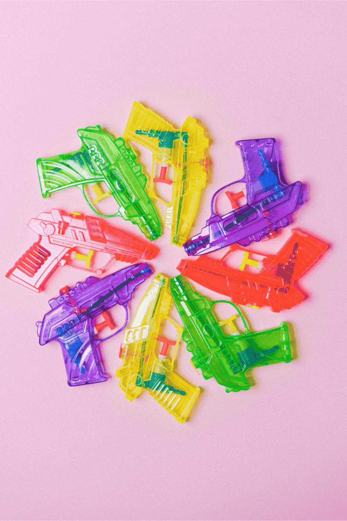 Colorful plastic toy water guns arranged in a circle on a pink background.
