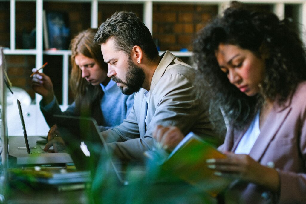 three people sitting at a desk looking at their laptop creens