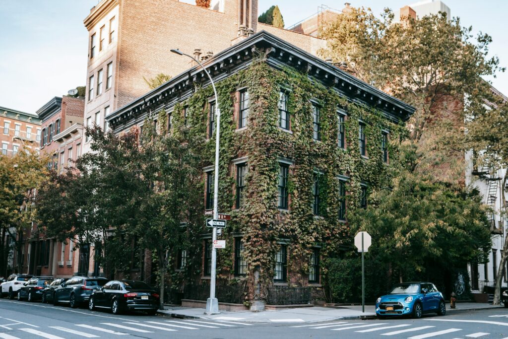 Historic ivy-covered apartment building on a street corner in Greenwich Village, New York City with parked cars and trees