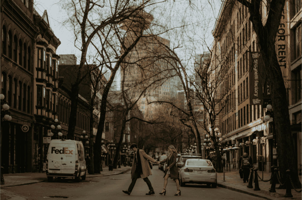 Couple holding hands while walking across a street in Gastown, Vancouver with the Harbour Centre tower in the background