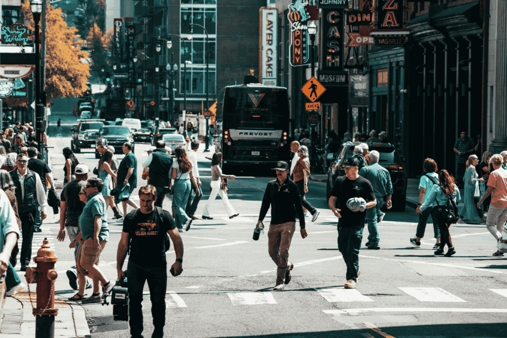 Busy street scene with crowds of people crossing the road near Broadway lined with neon signs, bars, and shops