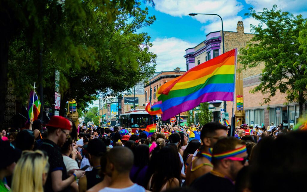 Large Pride parade with rainbow flags and a vibrant crowd marching through city streets celebrating LGBTQ+ pride.