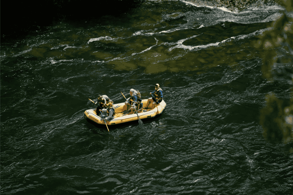 People rafting in a yellow inflatable boat, paddling together through flowing river water.