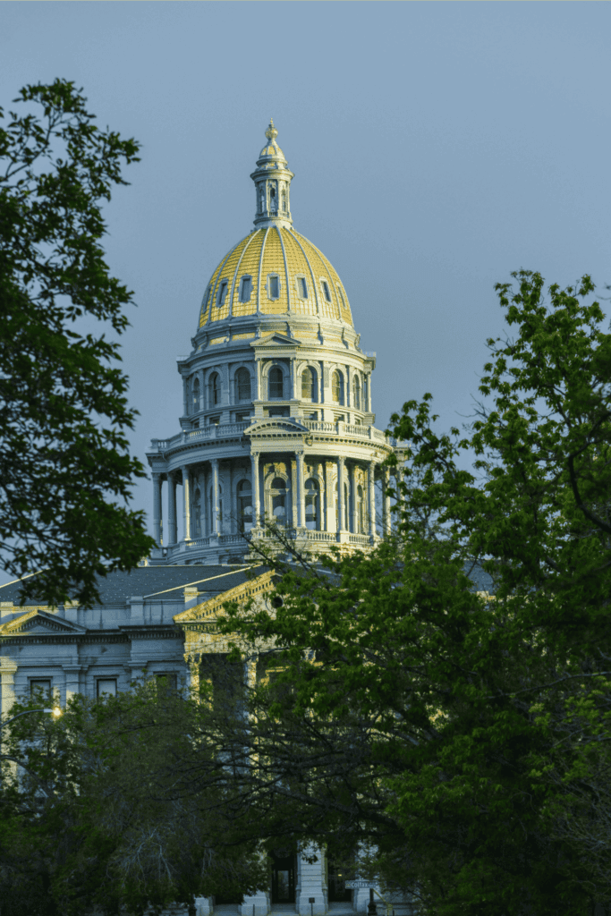 Colorado State Capitol building in Denver with its gold-domed roof framed by trees.