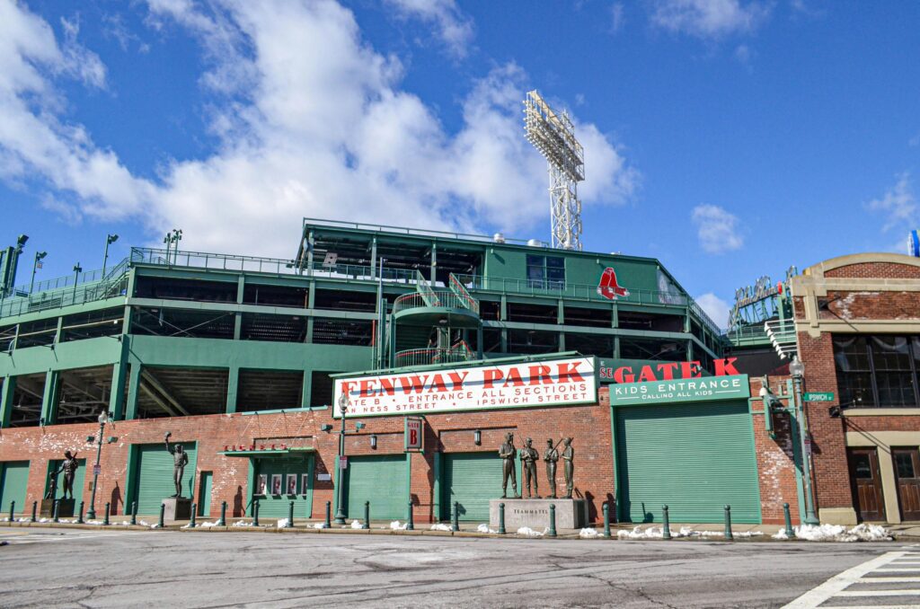 Fenway Park exterior view in Boston, Massachusetts, showing the iconic ballpark entrance with Red Sox signage and statues.