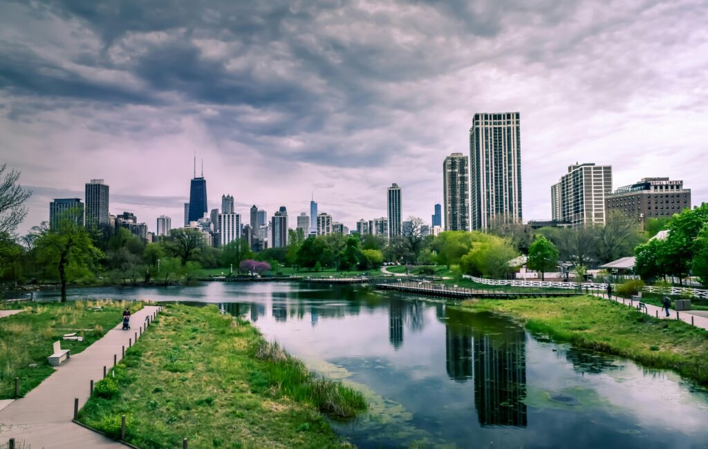Scenic view of the Chicago skyline from Lincoln Park with a pond and greenery in the foreground under a cloudy sky