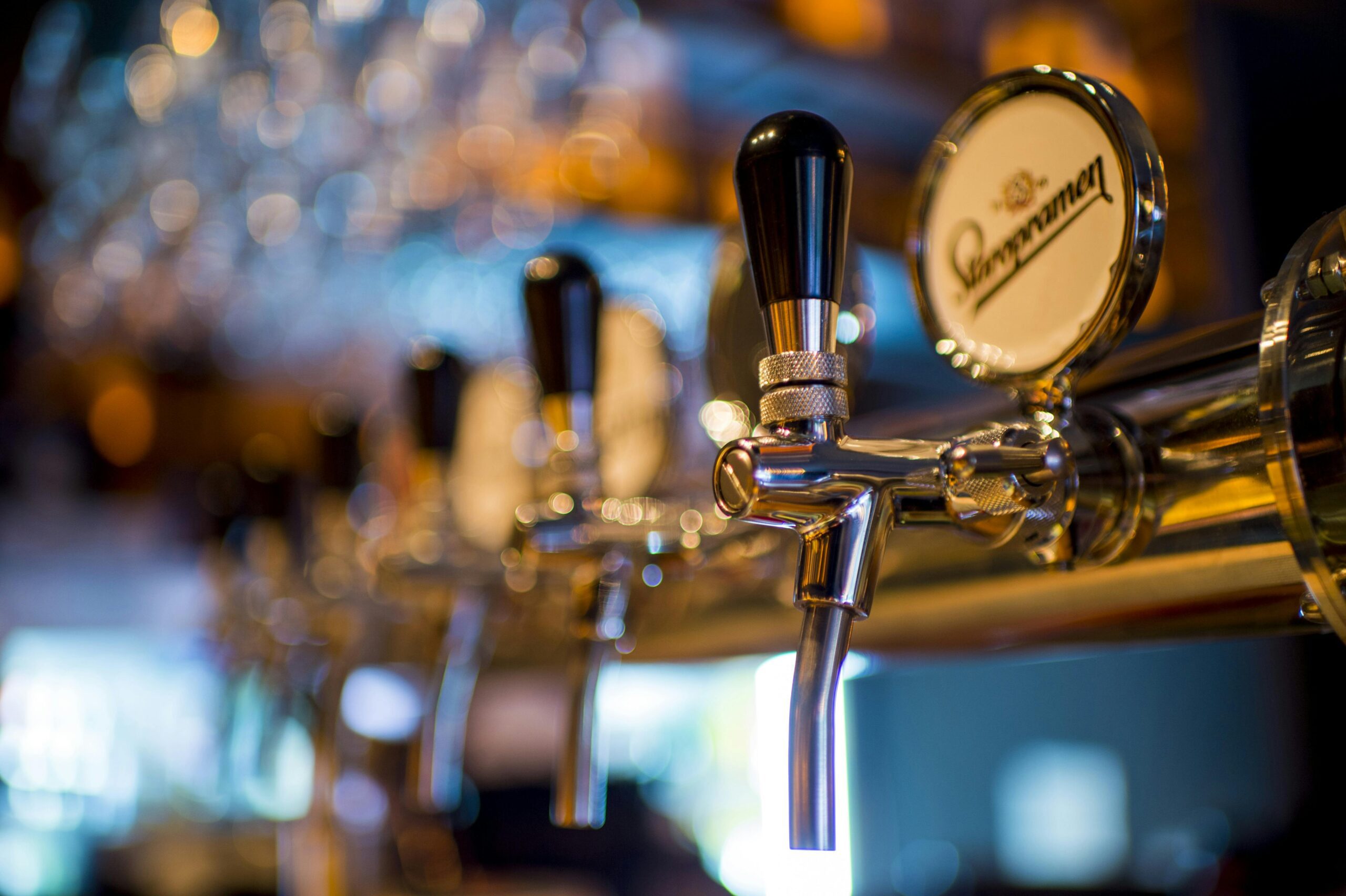 Beer taps at a bar with a close-up focus on shiny metal handles and blurred background lights.