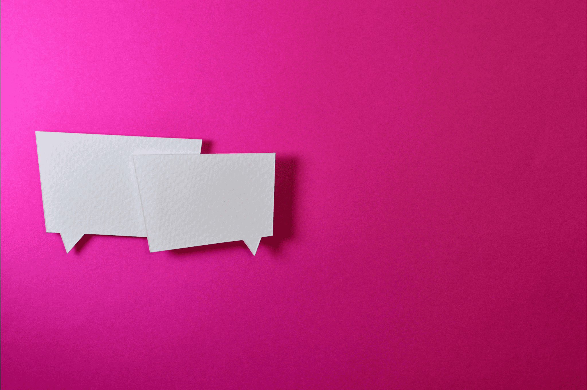 two white paper cutouts in the shape of speech bubbles placed on a bright pink background, symbolizing communication, conversation, or messaging