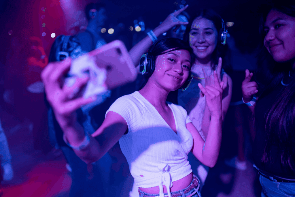 People enjoying a silent disco, smiling and taking selfies with wireless headphones glowing under vibrant lights