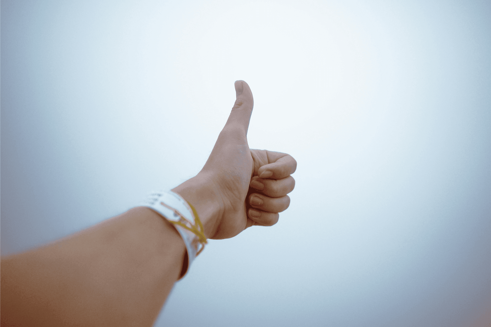 Hand giving a thumbs up gesture against a light background.