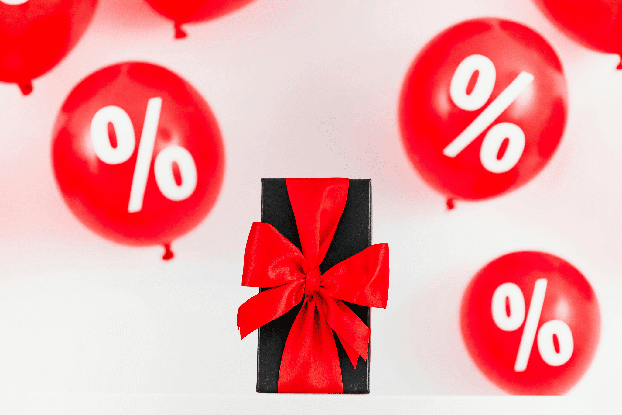 Black gift box with a red bow surrounded by red balloons with percentage signs.