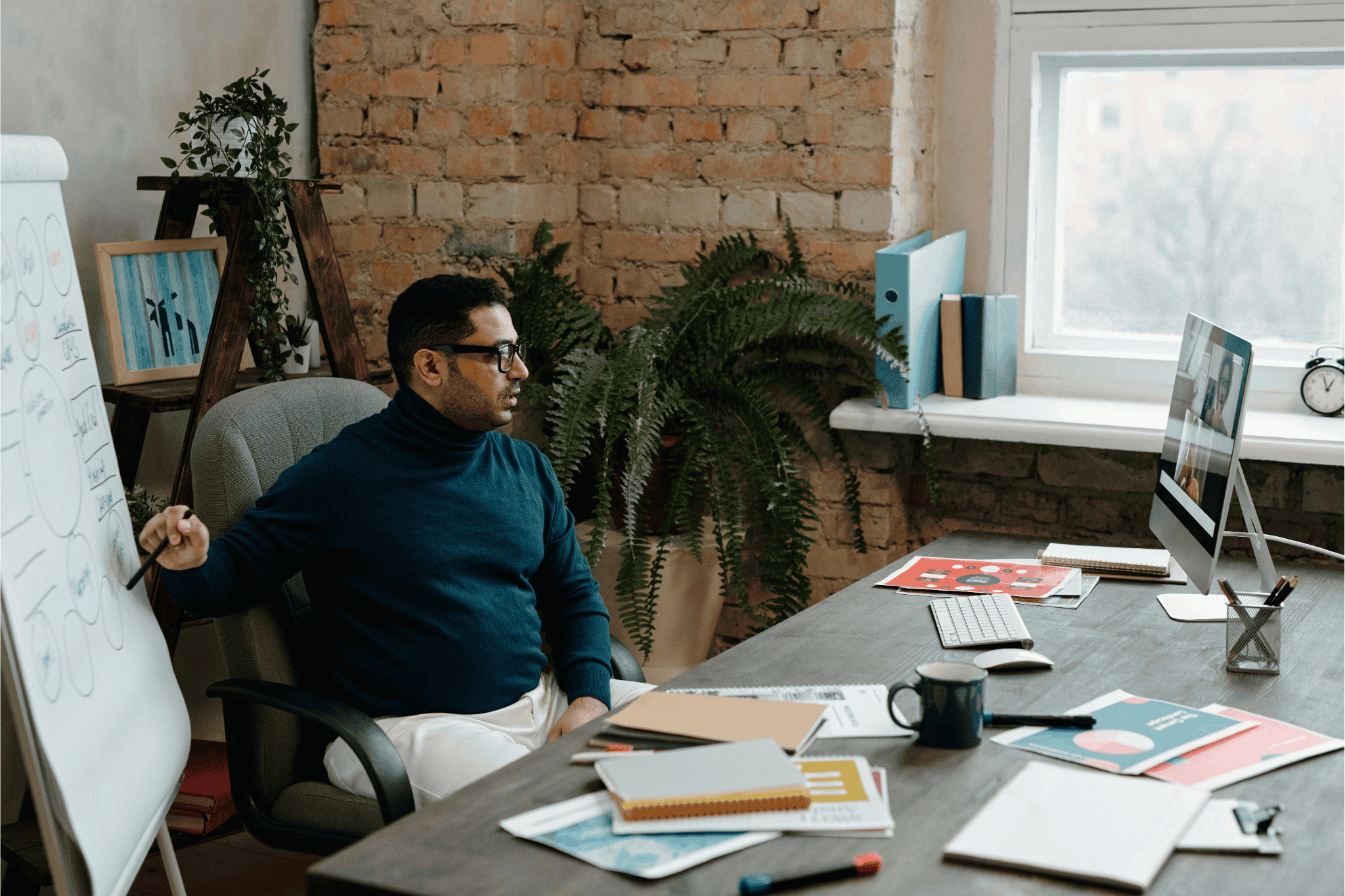 Man giving an online presentation from his office with notes and a whiteboard.
