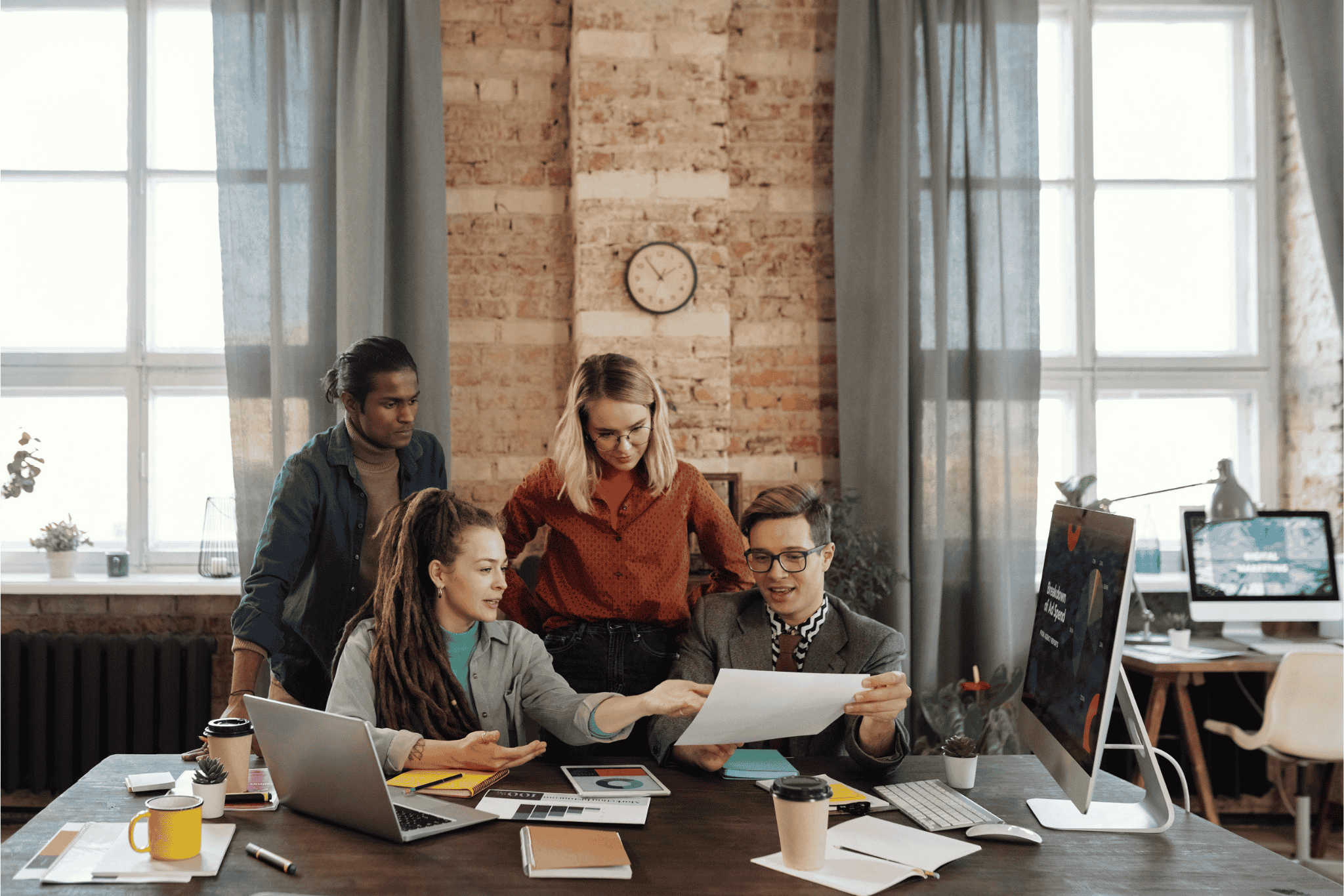 Team collaborating around a desk with laptops, documents, and coffee in a modern office.