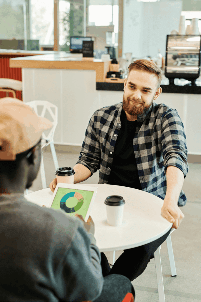 Two colleagues discussing data on a tablet over coffee in a casual meeting.
