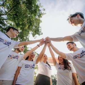 Group of people in matching shirts doing a team huddle outdoors.