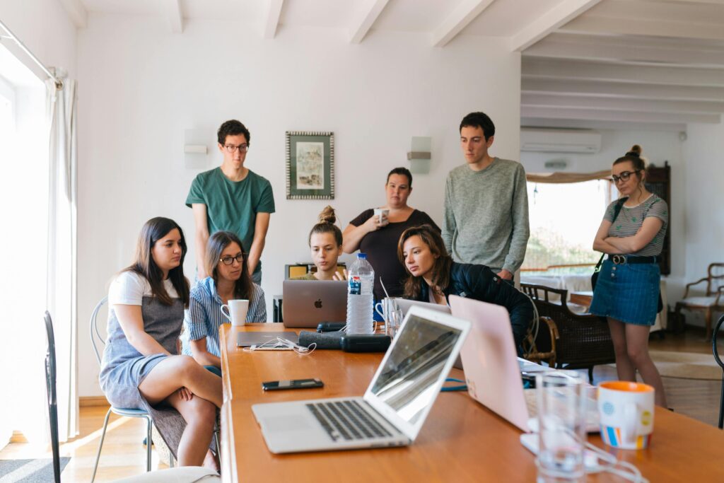 Group of young professionals gathered around laptops during a casual team meeting.

