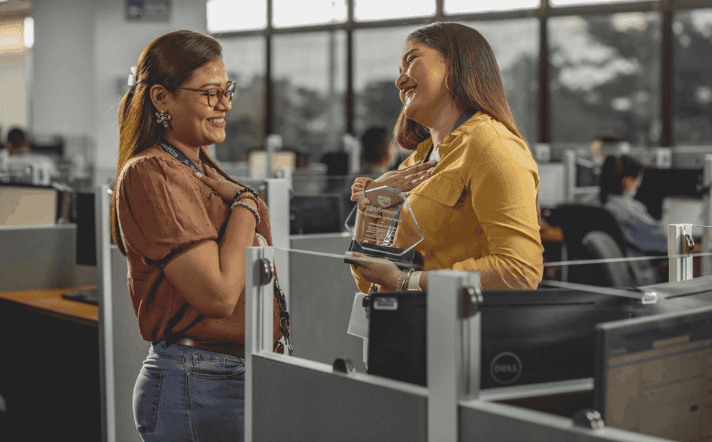 Employee receiving an award and sharing a joyful moment with a colleague in the office.
