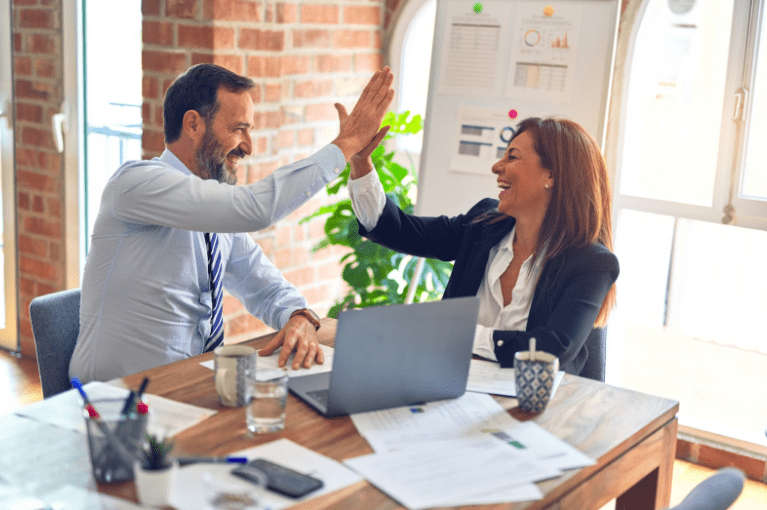man and woman sitting at the corner of a desk high-fiving