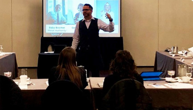 Man standing in front of a screen in a room of people teaching